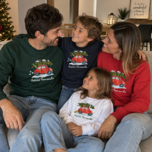 Familia de cuatro personas con sudaderas de Navidad personalizadas en verde, rojo, azul marino y blanco, con diseño de coche navideño y apellidos familiares, sentados juntos junto al árbol de Navidad.