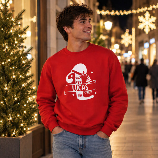 Chico con sudadera roja de Navidad personalizada con el nombre Lucas, en una calle con luces navideñas.